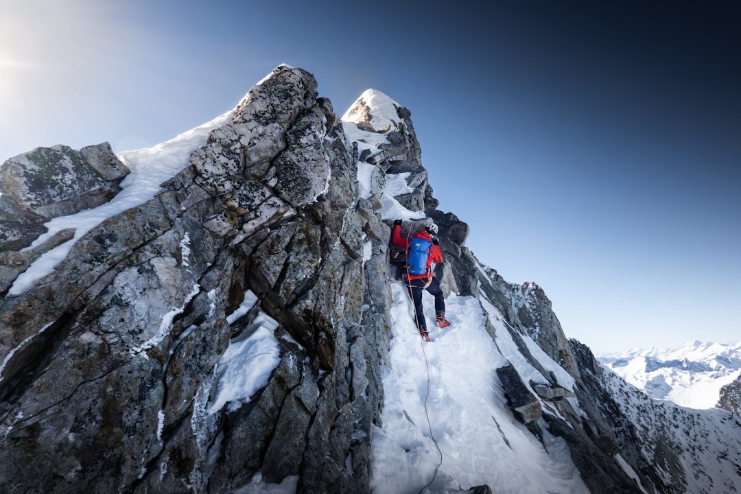 Mountaineer in red gear climbs snowy mountain ridge.